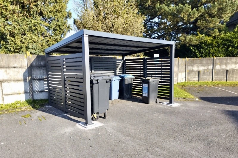 Abri en aluminium sur mesure EUROFACTORY avec brise-vues ajourés pour collectivités et espaces extérieurs, il abrite des poubelles.