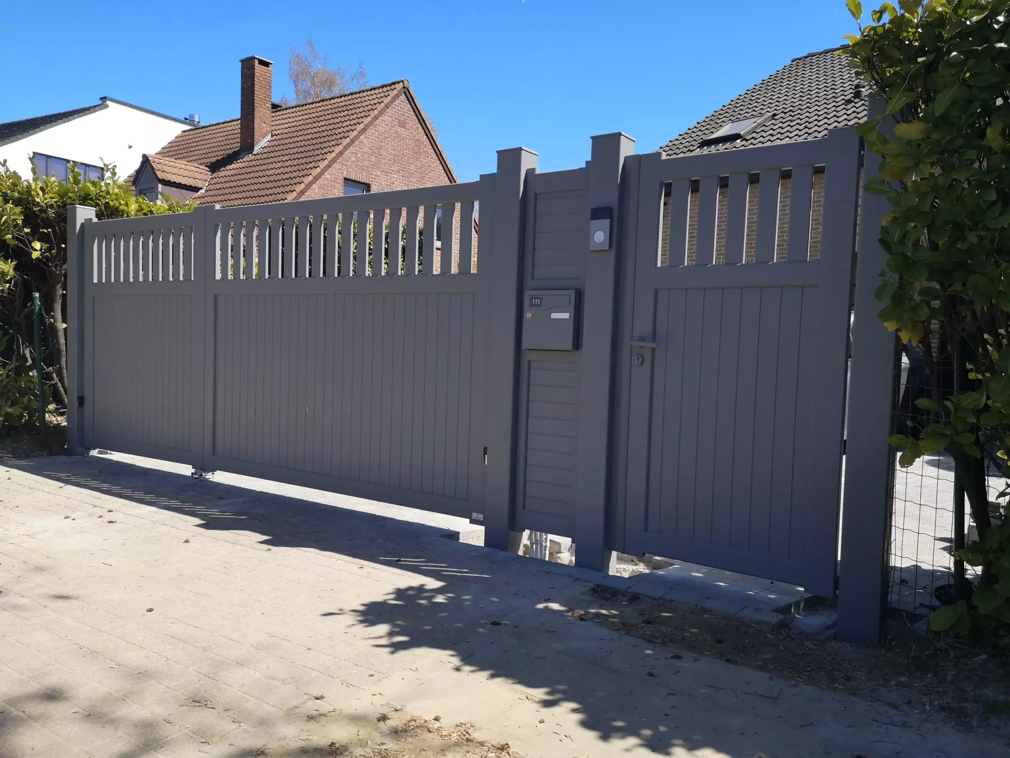 Portail battant à vantaux inégaux et portillon aluminium Chantilly gris à partie haute ajourée, séparés par un panneau de clôture à lames horizontales avec boîte aux lettres intégrée